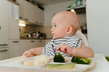 Feeding. Baby's first solid food. Baby boy eating vegetables. Child eating broccoli at home.