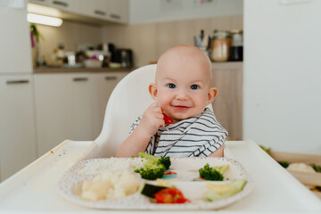 Feeding. Baby's first solid food. Baby boy eating vegetables. Child eating broccoli at home.