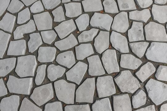 Continuous outdoor flagstone paving patterns with randomly cut cobblestone pieces in shades of grey, light grey, and charcoal. Monochromatic stone slabs for pavement and landscaping backgrounds.