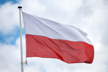 Polish flag fluttering in the wind with a blue sky and cloud background. 