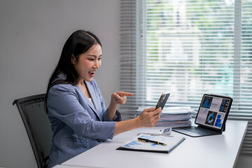 woman is sitting at a desk with a laptop and a cell phone