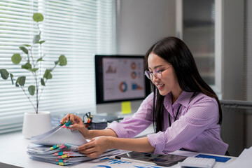 woman is sitting at a desk with a computer monitor and a stack of papers