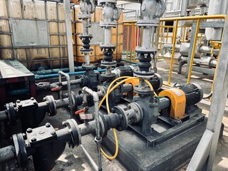 A wide-angle view of a pump system with multiple electric motors, pipes, and valves on a concrete platform, with large plastic tanks in the background.