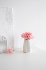 Pink chrysanthemums flowers in geometric vase, painting with white putty and candle stand on chest...