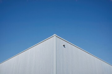 Fototapeta premium Three gray and white metal industrial structures with sunlight casting shadows, viewed from below against a clear blue sky