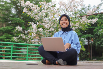 Portrait of Asian hijab woman sitting in city park, working on laptop