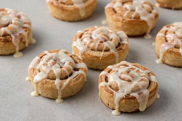 Delicious homemade cinnamon pastries topped with creamy vanilla glaze, presented on a neutral backdrop with ample space for text.