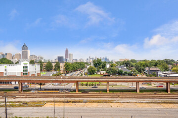 View of the city skyline from an elevated walkway overlooking train rail, trees and urban buildings.