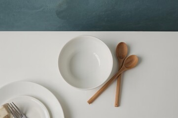 Plakat Top view of a clean white table featuring an empty bowl and wooden spoons, kitchen and cooking theme