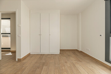 Bright empty room with glossy white wooden built-in wardrobes covering an entire wall, ready to be...