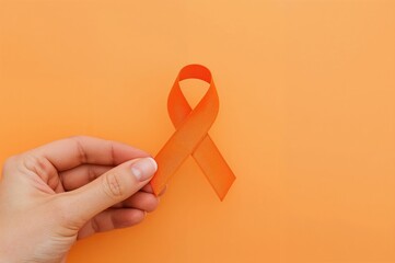 Close-up of a hand holding an orange ribbon symbolizing kidney cancer and leukemia awareness with ample copy space