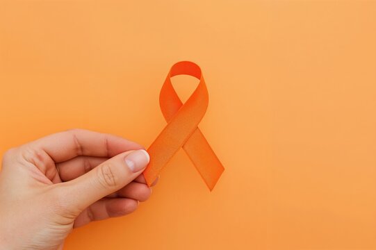 Close-up of a hand holding an orange ribbon symbolizing kidney cancer and leukemia awareness with ample copy space