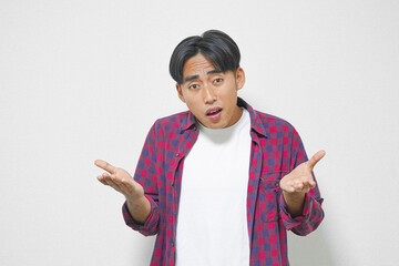 Young man with surprised expression, gesturing with open hands, wearing a red and blue plaid shirt...