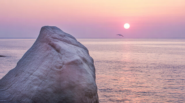 Serene beach sunset with soft pastel hues and large rock formation - Powered by Adobe