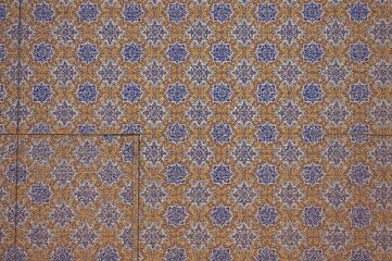 Historic structure decorated with vibrant blue and yellow tile mosaics on brick, illuminated by sunlight