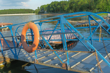 Rustic blue painted metal pier with lifebuoy tied on railing leading to peaceful river with moored...