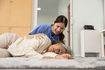 Asian Elderly woman lying on floor unconscious with worried nurse providing emergency care in home...