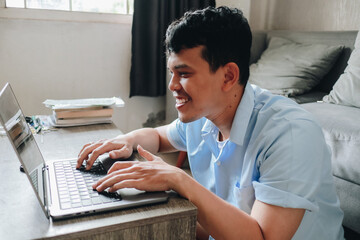 Young Man Working on Laptop at Home in a Cozy Room While Smiling at His Screen