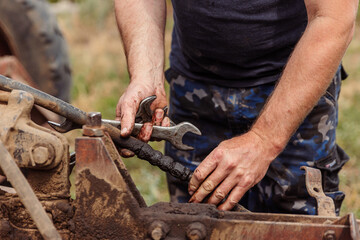 A mechanic with tools in his hands connects the hydraulic system of a trailer to an old tractor, close-up.