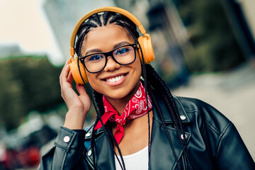 Young woman with braided hair enjoying music outdoors with headphones and a cheerful smile in a...