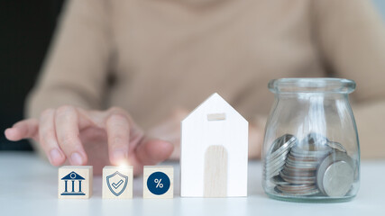 Wooden house model with glass jar of coins and banking icons, symbolizing mortgage loan, property...