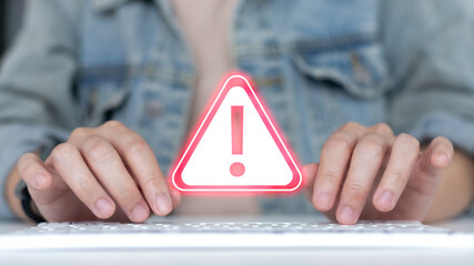 Hands typing on a keyboard with a warning alert icon, symbolizing cybersecurity risk, online threat, data breach, fraud detection, hacking attempt, and digital system error notification.