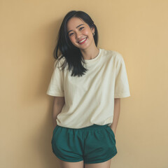 Fototapeta premium A Japanese woman in a white t-shirt and shorts poses casually against an orange yellow background, reflecting a relaxed summer fashion vibe.