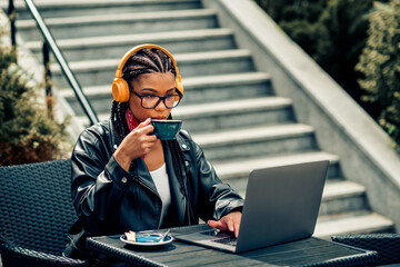 Young woman sipping coffee while working outdoors on a laptop enjoying a peaceful urban day