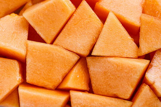 Closeup, overhead shot of a pile of diced cantaloupe chunks, showcasing the vibrant orange color and juicy texture.
