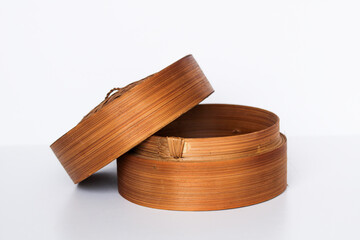 A side-view of a traditional bamboo steamer with its lid open and resting on the side, on a white background.