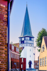Symbol of stability above town life — the tower of St Nicolas Church rises behind red-roofed...