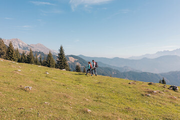 Two hikers, a man and a woman, walking over a grassy slope with a scenic view of misty mountains...
