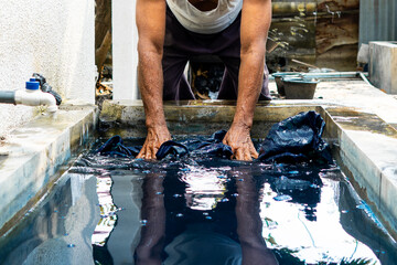 Close-up of artisan hands immersing indonesian batik cloth in an indigo dye bath. Process shot...