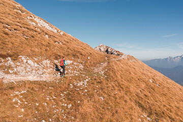 Woman is trekking along a rocky path on a mountain with golden grass and distant peaks under a...