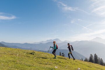 Two hikers, a man and a woman, walking over a grassy slope with a scenic view of misty mountains...