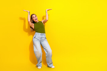 Cheerful young woman posing with enthusiasm in a casual khaki top and jeans against vibrant yellow...