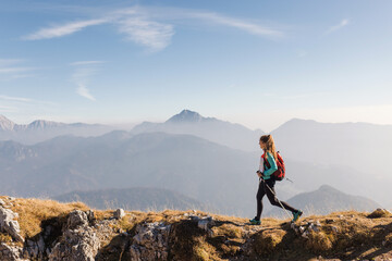 Woman hikes on a mountain ridge during sunset, surrounded by impressive peaks and valleys in the...