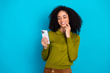 Fototapeta premium Happy young African American woman in casual khaki shirt smiling and using smartphone on a blue background