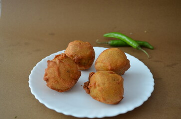 Crispy aloo bonda served in a plate on a brown background. A traditional South Indian snack made with spiced mashed potato balls coated in gram flour batter and deep-fried until golden.
