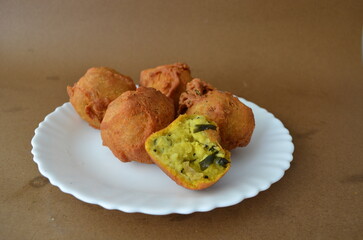 Crispy aloo bonda served in a plate on a brown background. A traditional South Indian snack made with spiced mashed potato balls coated in gram flour batter and deep-fried until golden.