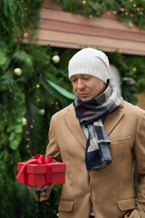 Mans holding red gift at Christmas fairy. Xmas bazaar market. Holiday spirit. Close up.
