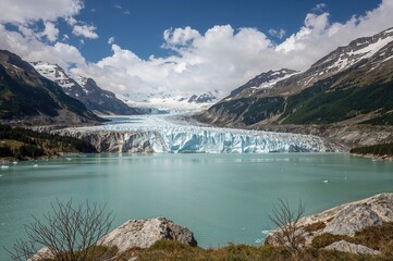 Obraz premium Glacier-fed lake signaling the start of a major river amid alpine peaks, featuring protective ice coverings to minimize meltwater