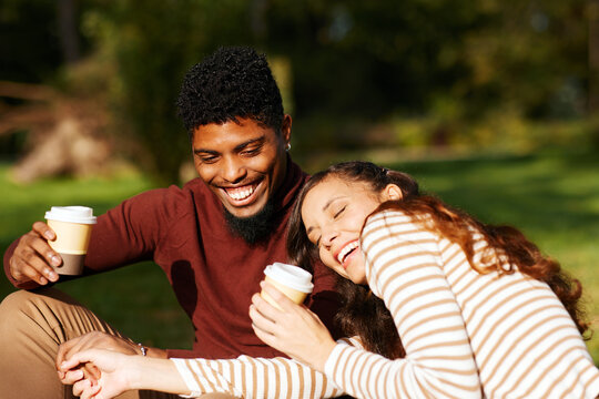 Happy multi-ethnic couple laughing and drinking coffee outdoors in autumn - Powered by Adobe