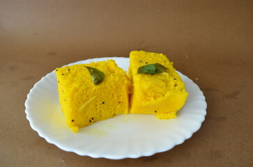 Two pieces of soft and fluffy dhokla. A light and spongy Gujarati snack made with fermented gram flour batter, steamed to perfection, and garnished with mustard seeds, curry leaves, and green chilies.