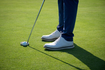 Golfer putting ball on green, closeup of feet and club