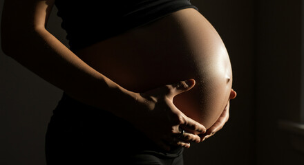 Close-up of a pregnant woman's belly with hands gently resting on her abdomen, bathed in soft, natural light.