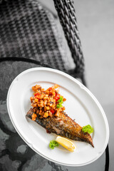 Grilled fish fillet topped with tomato-onion salsa, garnished with lemon and parsley, served on a white plate in a restaurant setting