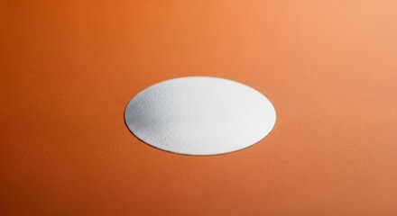 Silver oval sticker on textured orange surface, simple and minimal