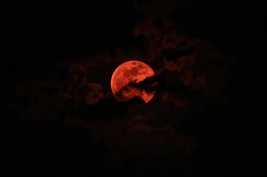 Crimson lunar eclipse against a dark cloudy sky, authentic full red moon captured