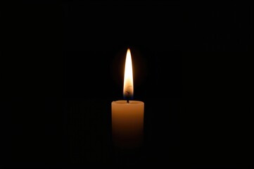 A lone candle glowing against a pitch-black backdrop.